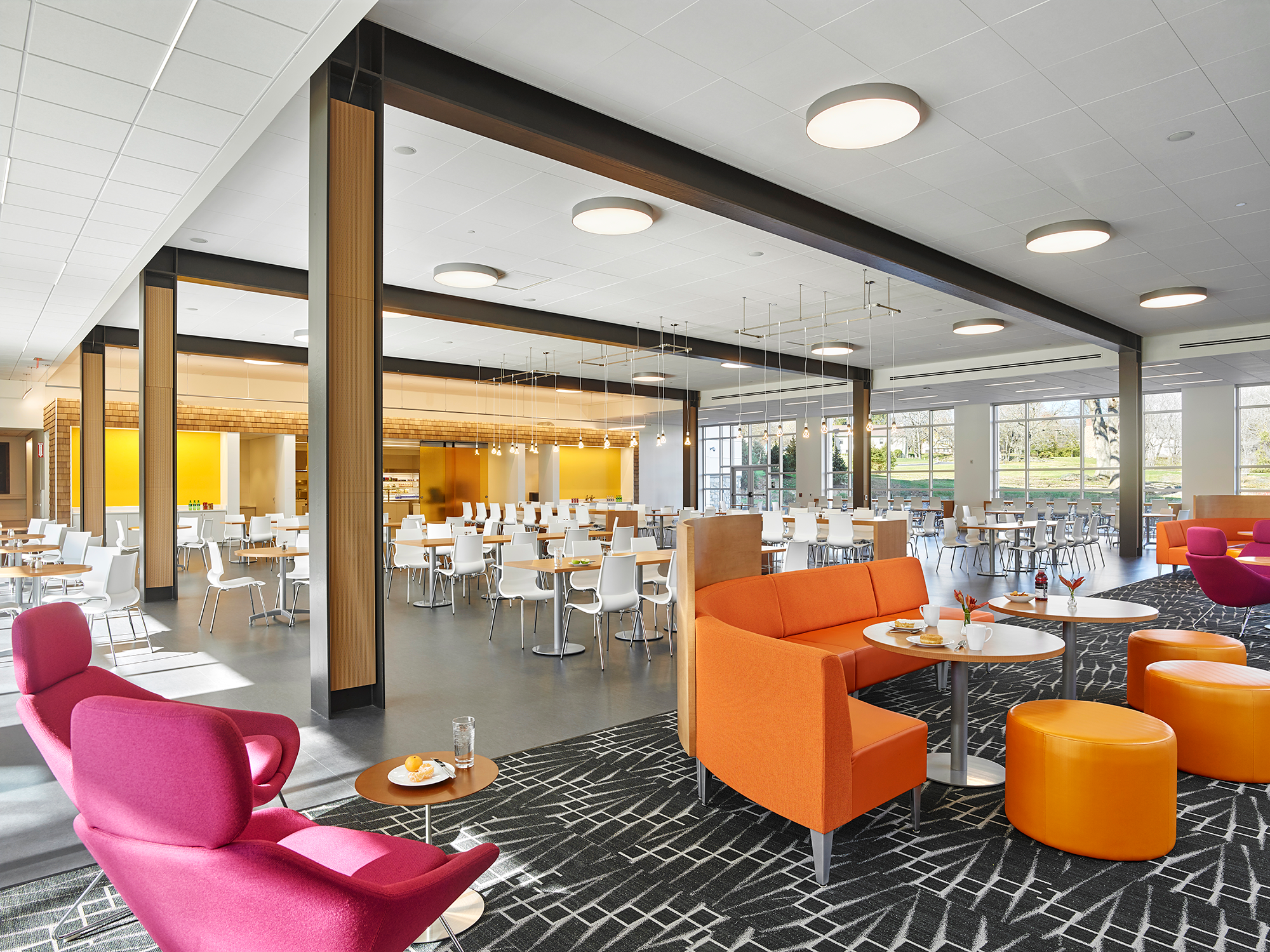 Seating area for a cafeteria with wooden beams along the ceiling. Some chairs are pink and orange.