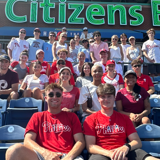 A group of young professionals wearing baseball t-shirts are attending a Philadelphia Phillies game