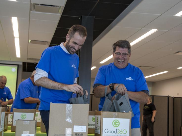 Two men in blue company shirts are packing care packages for Good360