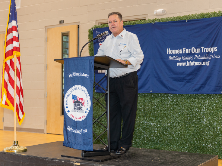 A CertainTeed employee is speaking at a Homes For Our Troops podium at an event.