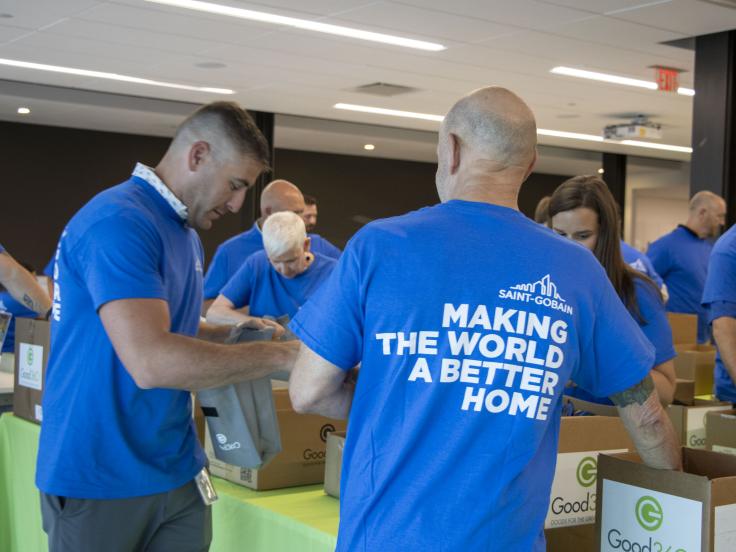 People wearing shirts that say "Making The World A Better Home" packing kits from cardboard boxes with Good360 logos on them.