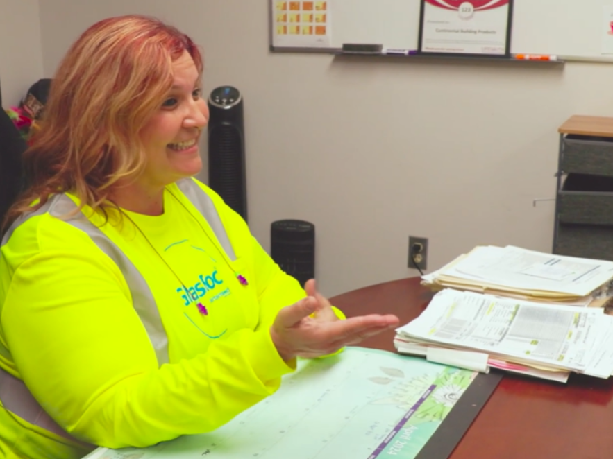 An HR specialist wearing yellow safety gear speaks with an employee in her office