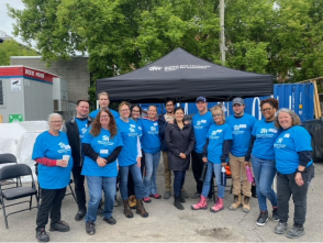 A group of people pose for a photo underneath a Habitat for Humanity tent wearing matching shirts