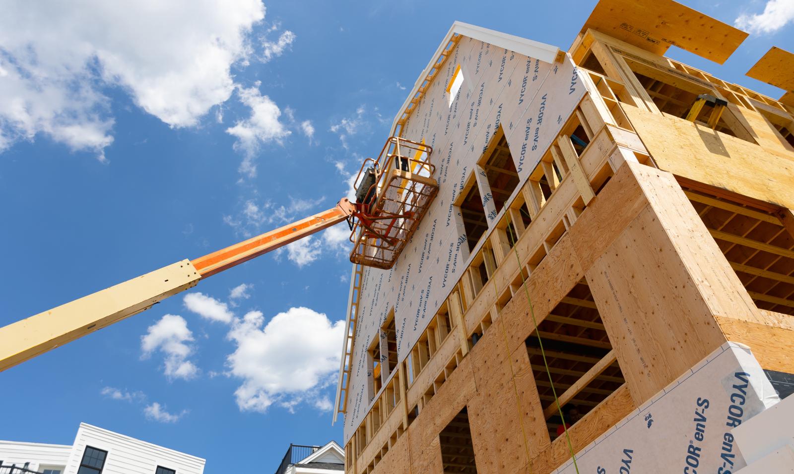 Home under construction, bare siding showing with a mechanical crane reaching up alongside the structure.