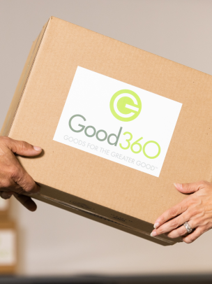 Two sets of hands are holding a cardboard box that has a Good360 sticker on it 