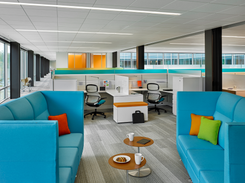 Two light blue couches face one another with cubicles in the background. 